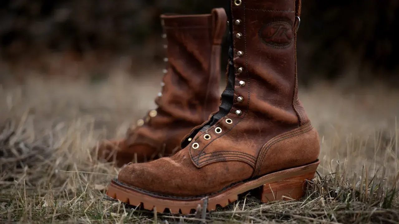 Two brown leather work boots with a lug sole, meaning a thick, rugged sole with deep treads for excellent grip, stand in dry grass.