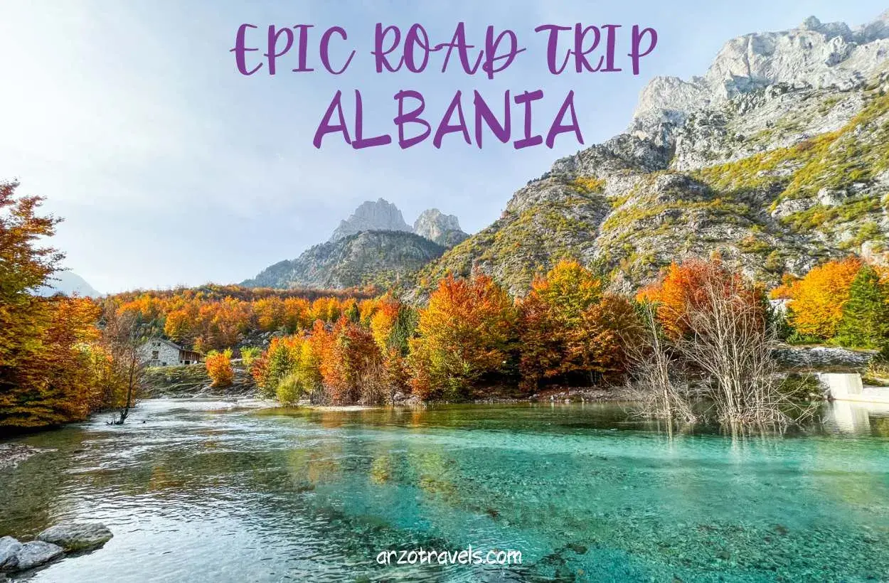 An epic road trip through Albania reveals a stunning turquoise river flowing past a stone house, with mountains and vibrant autumn foliage.