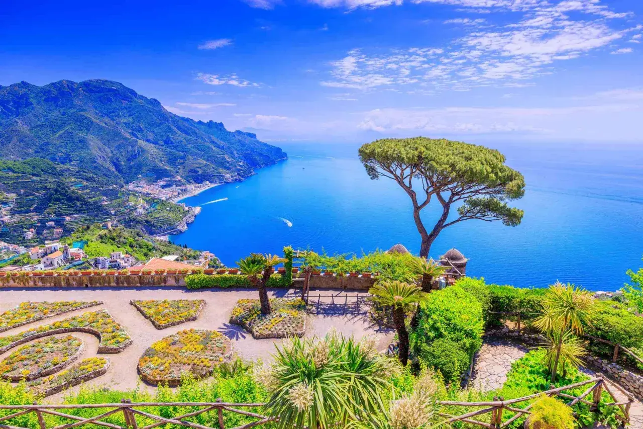 A stunning view of the Amalfi Coast, a perfect destination for a trip from Naples. Lush gardens overlook the sparkling blue sea and dramatic cliffs.