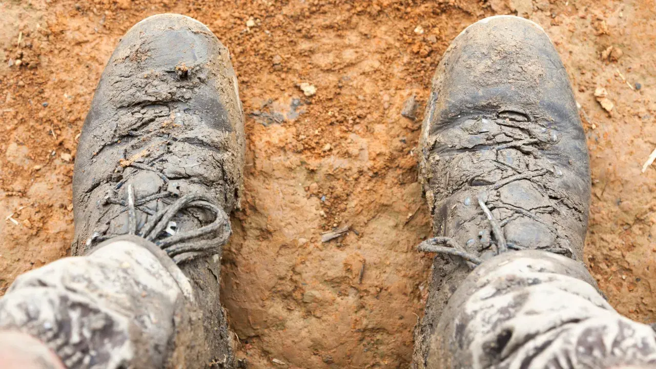 Mud-caked boots stand in dirt. The question "do boots shrink over time?" lingers as these boots look like they've seen many adventures.