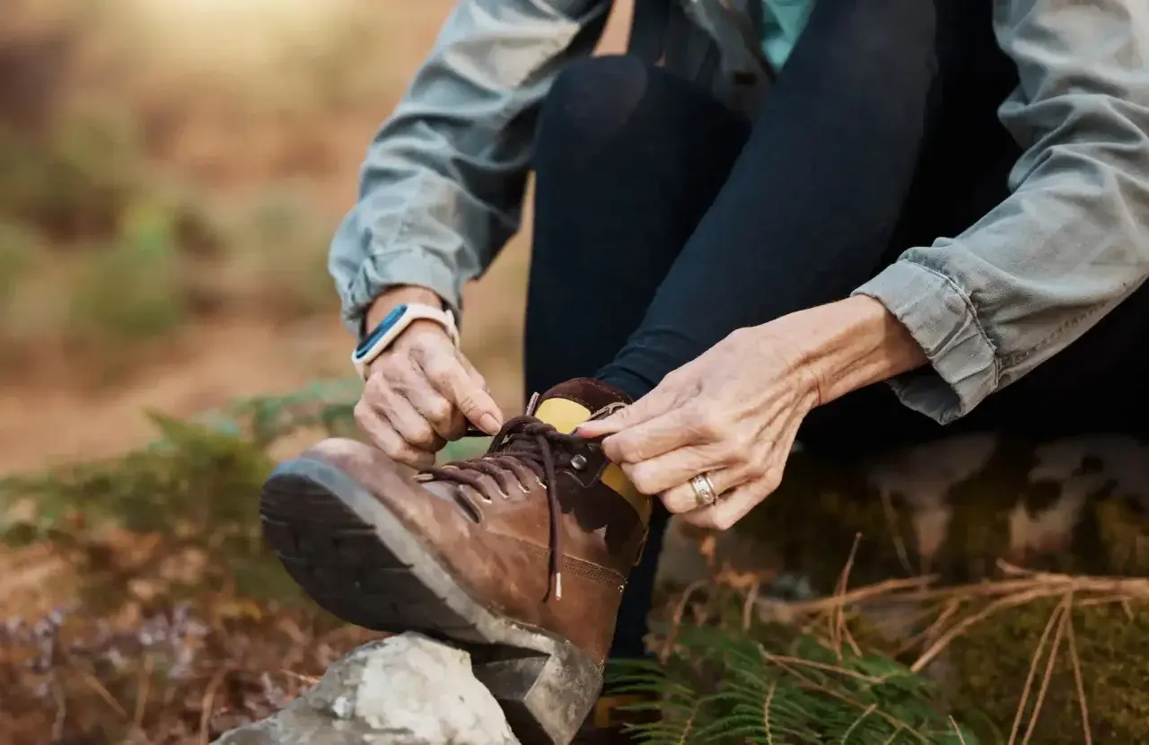 A person demonstrates how to lace boots, preparing for an outdoor adventure.
