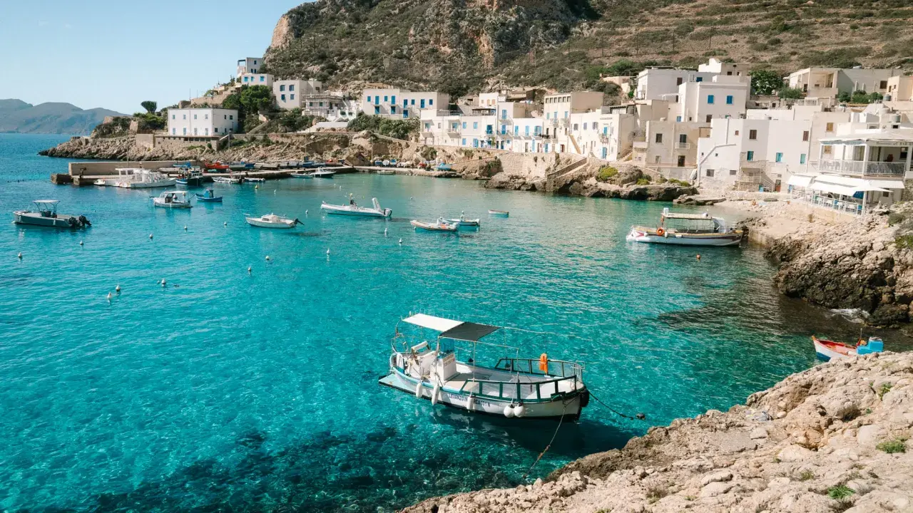 A picturesque harbor with white buildings and boats, showcasing one of the top places to see in Sicily.