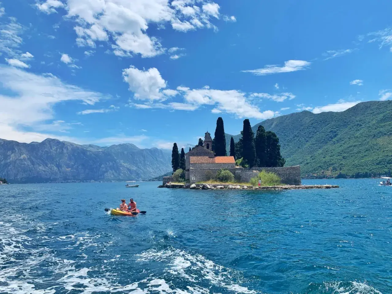 Kayaking in Montenegro's Bay of Kotor, a perfect spot for any trip planner. Mountains and a church on an island create a stunning backdrop.