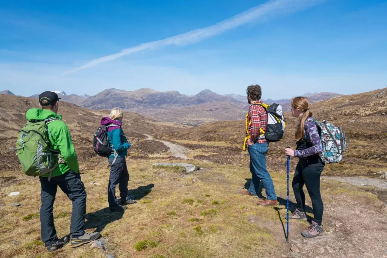Four hikers enjoy a scenic view on Scotland hiking trips, with mountains stretching into the distance under a clear blue sky.