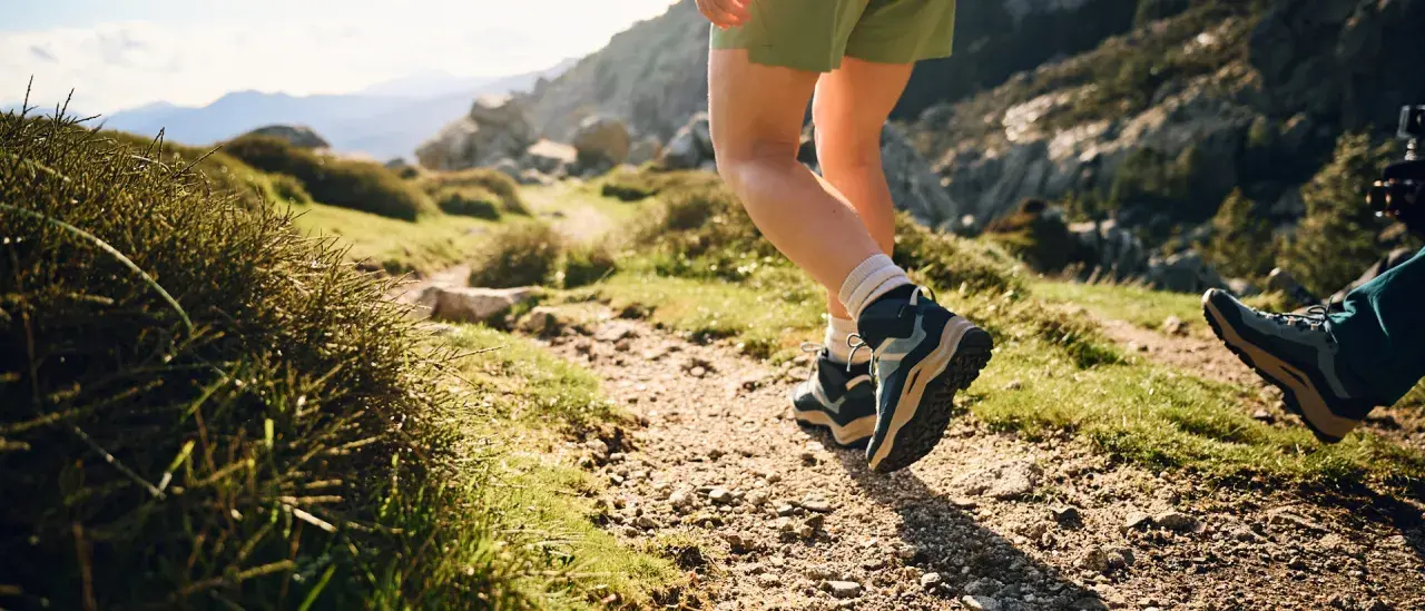 Hiking boots, one leather, one synthetic, tread a rocky path through a sun-drenched mountain landscape.