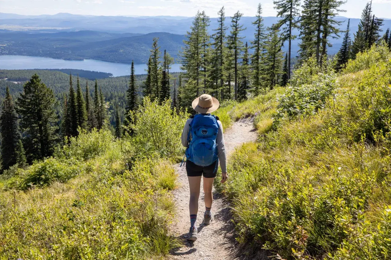 A hiker with a blue backpack walks on a trail, enjoying one of the best long hikes in the world with a stunning lake and mountain view.