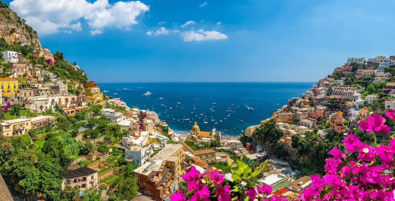 Colorful houses cascade down a cliffside to the sea, a picturesque view of the Amalfi Coast, a popular destination from Naples Airport.