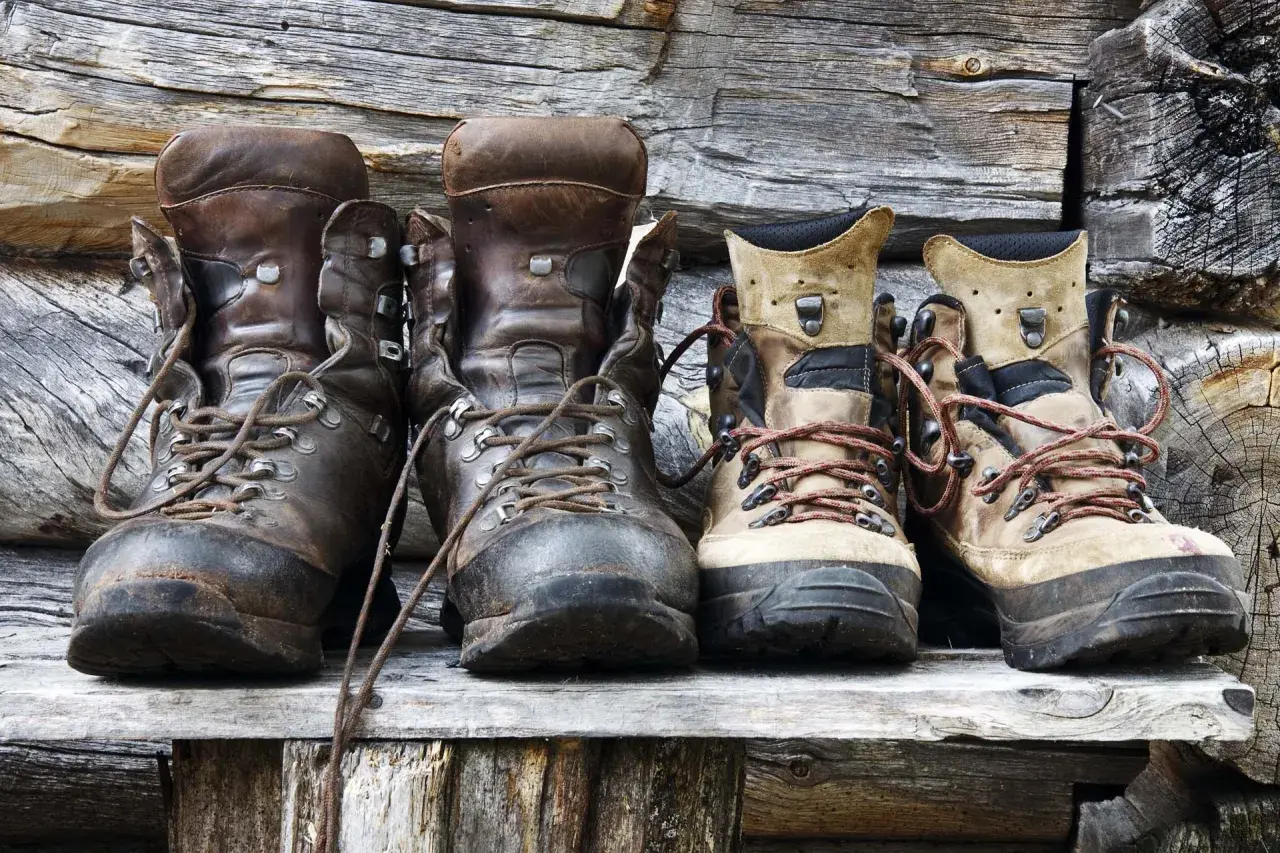 Four pairs of hiking boots, two dark brown leather and two tan, sit on a wooden shelf. Considering if you should size up in hiking shoes?