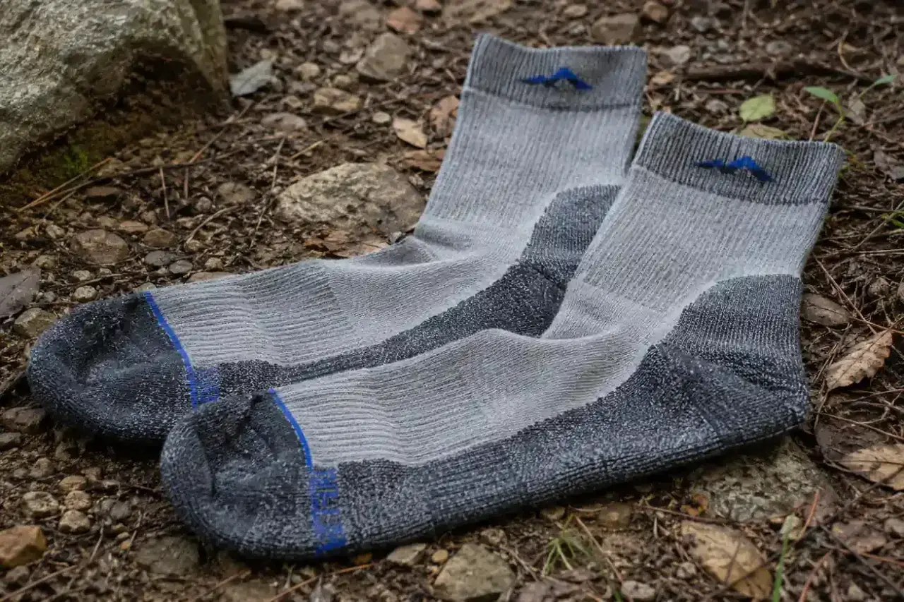 Gray hiking socks with blue mountain logos lie on the forest floor. Learn how to choose hiking socks for comfort and support.