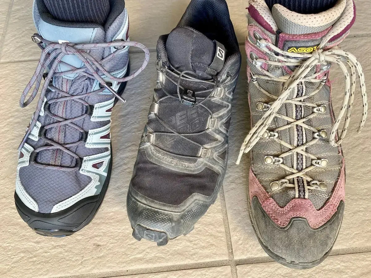 Three hiking boots: a low-cut grey boot, a mid-cut black boot, and a high-cut grey and pink boot.