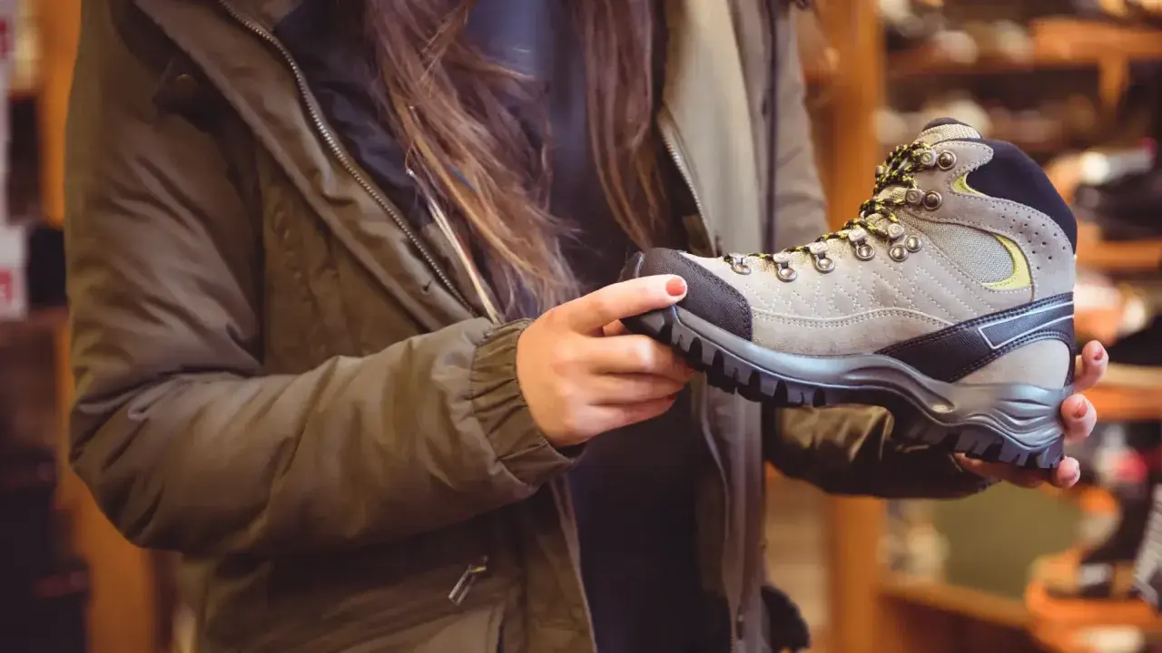 A person in a green jacket holds a hiking boot, considering if boots should fit snug or loose for comfort on the trail.