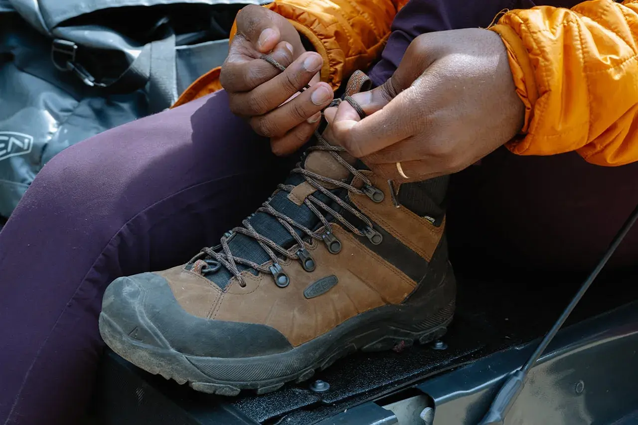 Close-up of hands tying brown hiking boots, demonstrating how to tie hiking boots for an outdoor adventure.