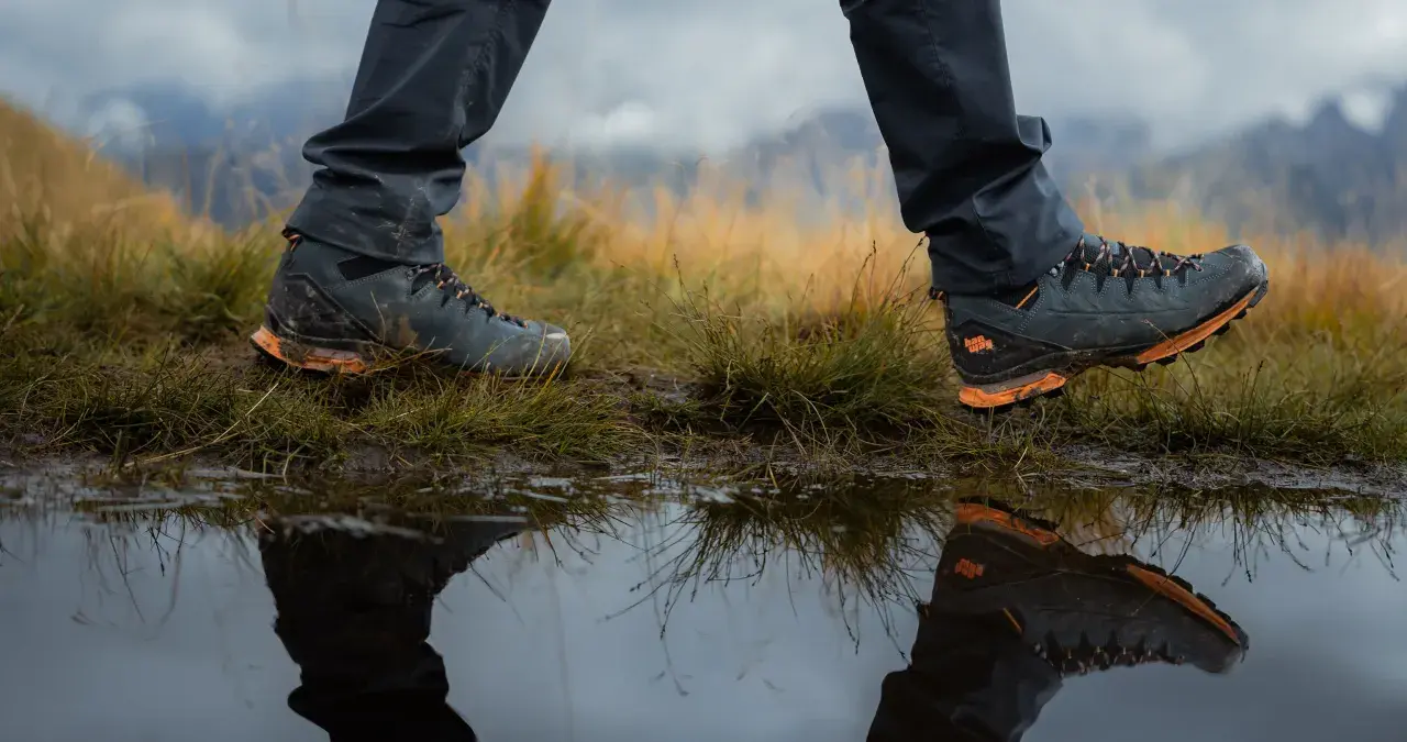 Hiking boots reflected in a puddle. Learn how to get your shoes to stop squeaking on your next adventure.