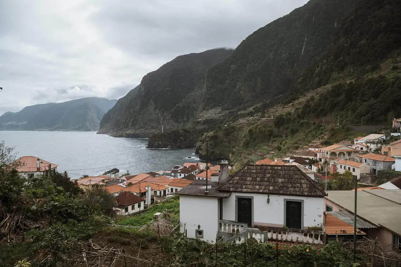 Coastal village with red-tiled roofs nestled against lush green mountains. A perfect place to stay in Madeira, offering stunning ocean views.