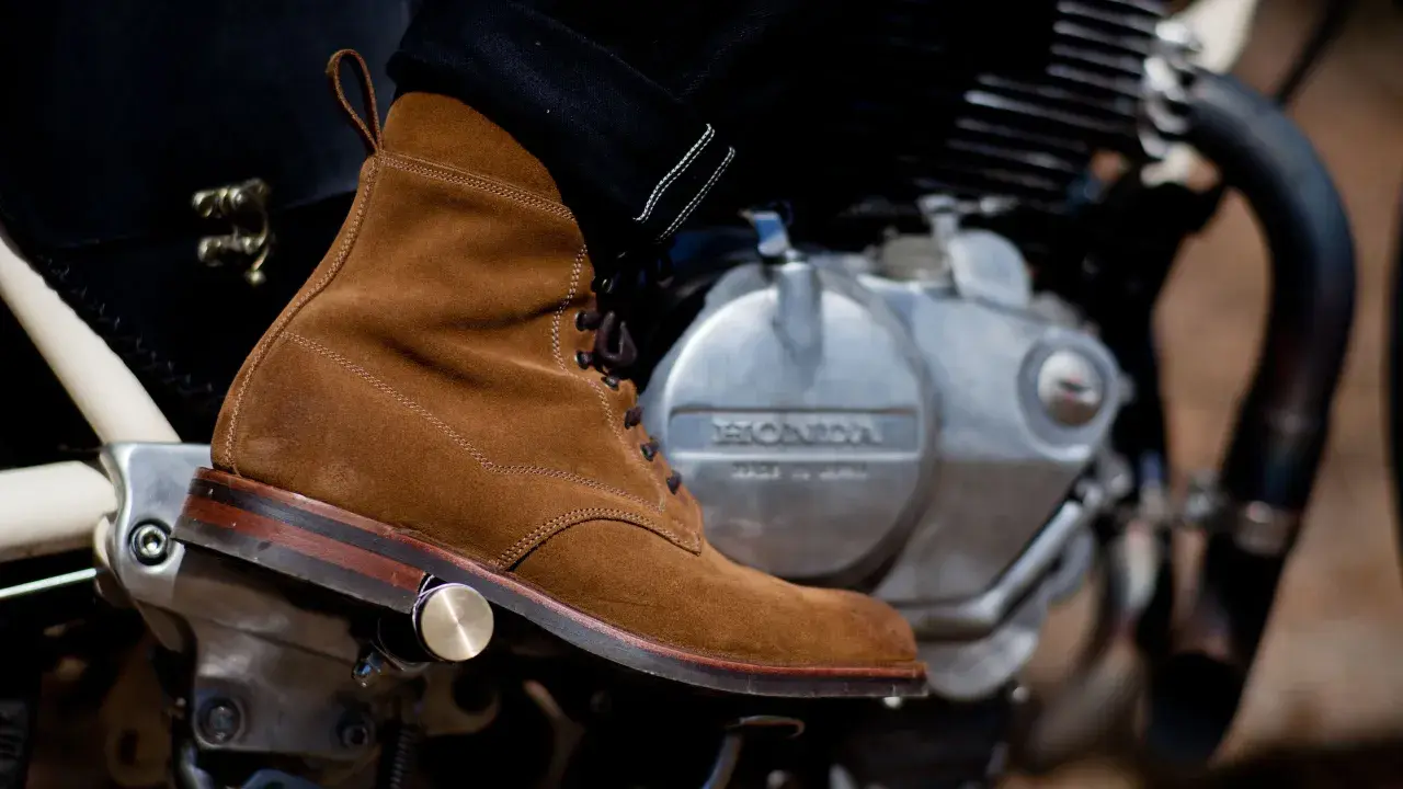 A suede boot rests on a motorcycle engine, ready for a ride. Learn how to walk in boots like these for style and comfort.