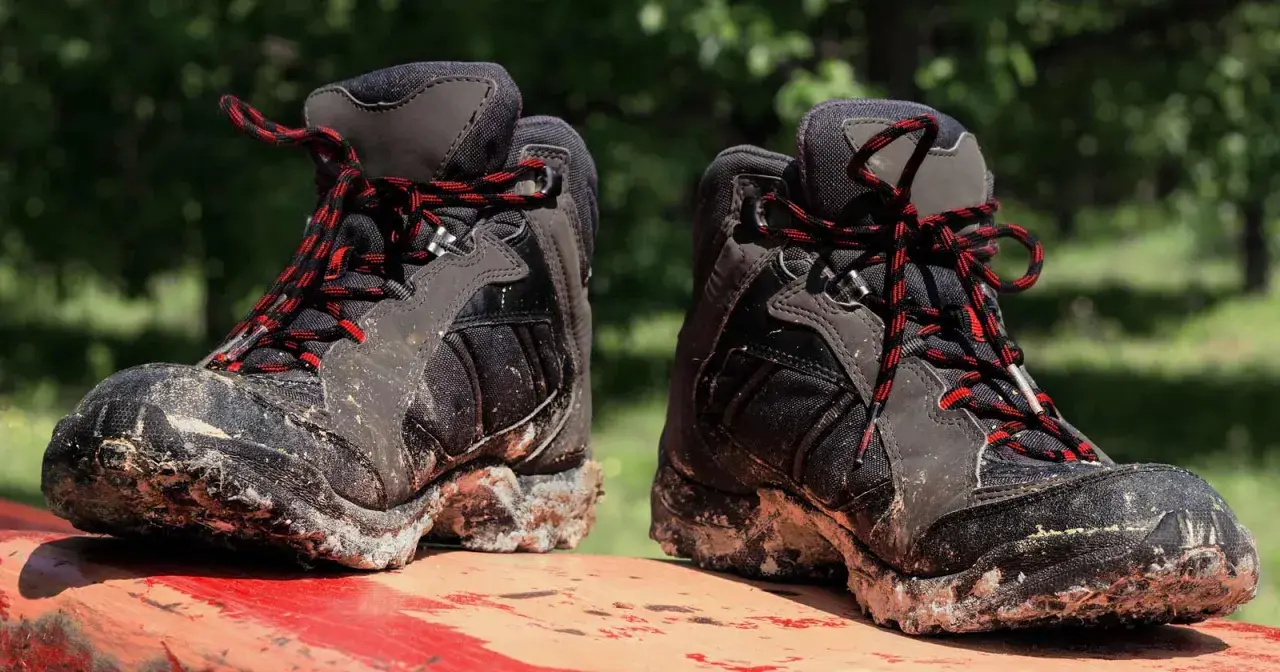Mud-caked hiking boots with red and black laces sit on a red surface. These boots show signs of heavy use, hinting at how long do hiking boots last.