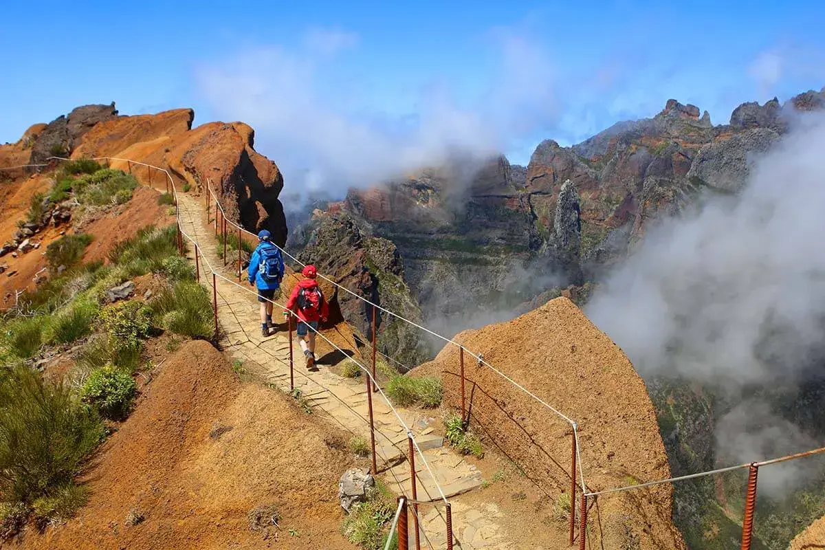 Hikers on a mountain path, a perfect example of things to do in Madeira. Dramatic cliffs and clouds surround them.