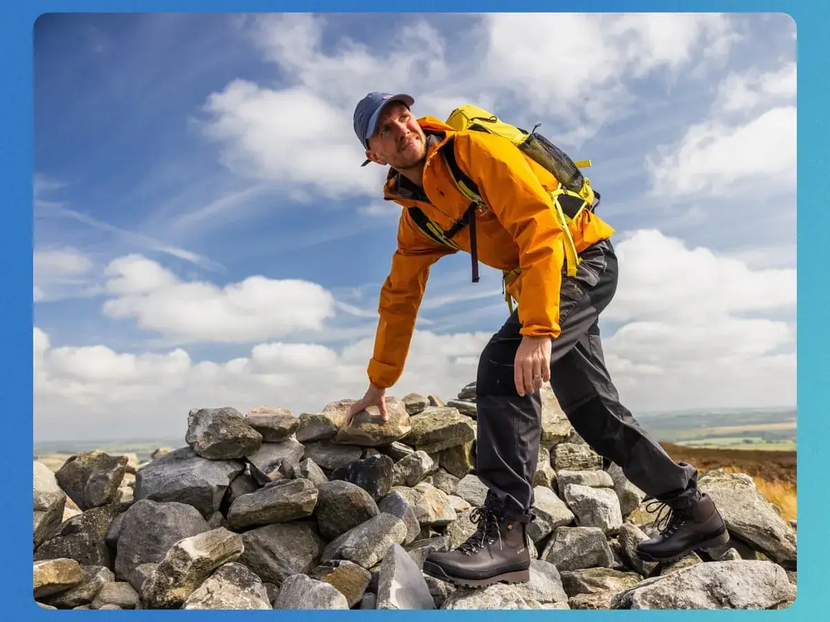 Man in orange jacket and sturdy boots navigates a rocky path, demonstrating how to walk in boots on uneven terrain.