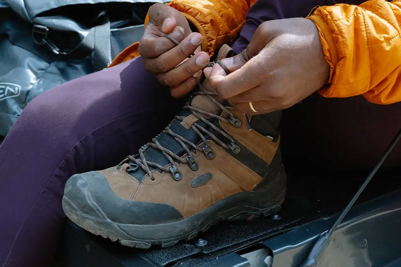 Hands tying brown hiking boots, a crucial step for any adventure. Learn how to tie hiking boots securely for a comfortable trek.