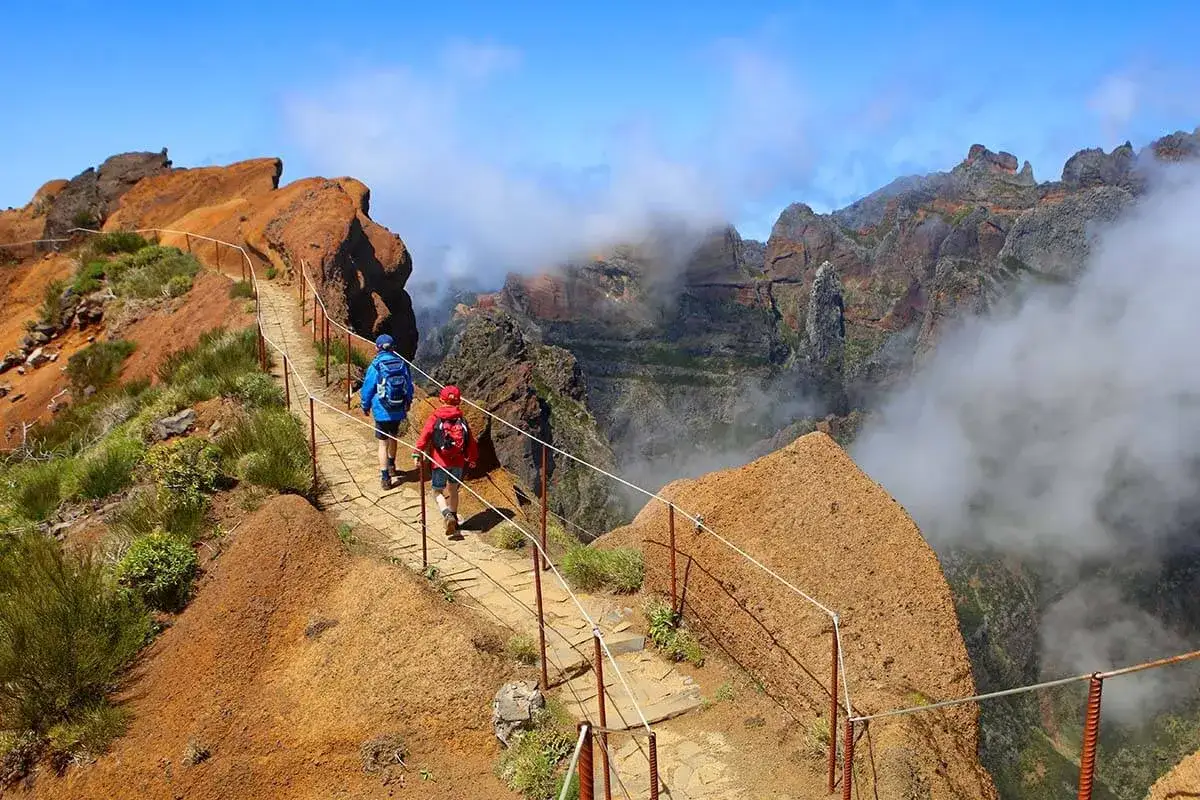 Hikers on a mountain path, a classic of things to do in Madeira, with dramatic cliffs and clouds below.