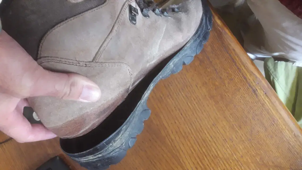A hand lifts a hiking boot, revealing the sole has detached. This illustrates why shoes fall apart when not worn: adhesives degrade over time.