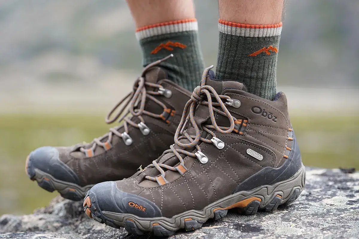 Brown Oboz hiking boots with green socks featuring an orange mountain logo. These socks are essential for comfortable hiking.