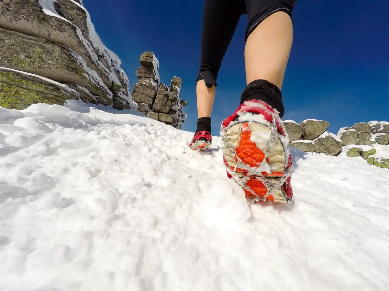 Traction-enhanced running shoes, perfect shoes to wear in winter besides boots, navigate snowy mountain terrain under a clear blue sky.