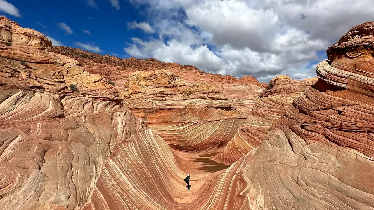 A lone hiker explores the surreal, wavy sandstone formations of The Wave, a dream destination for the best long hikes in the world.
