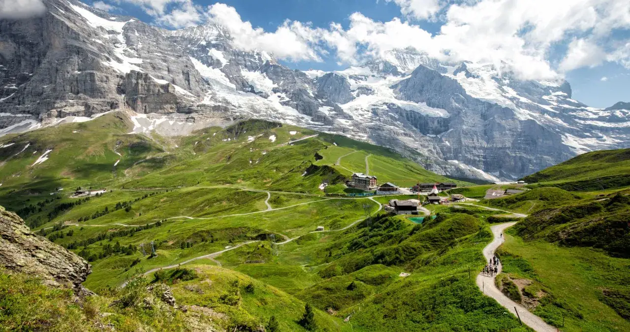 Hikers enjoy a scenic path through lush green valleys with snow-capped mountains in the background, a perfect day for hiking in Switzerland.