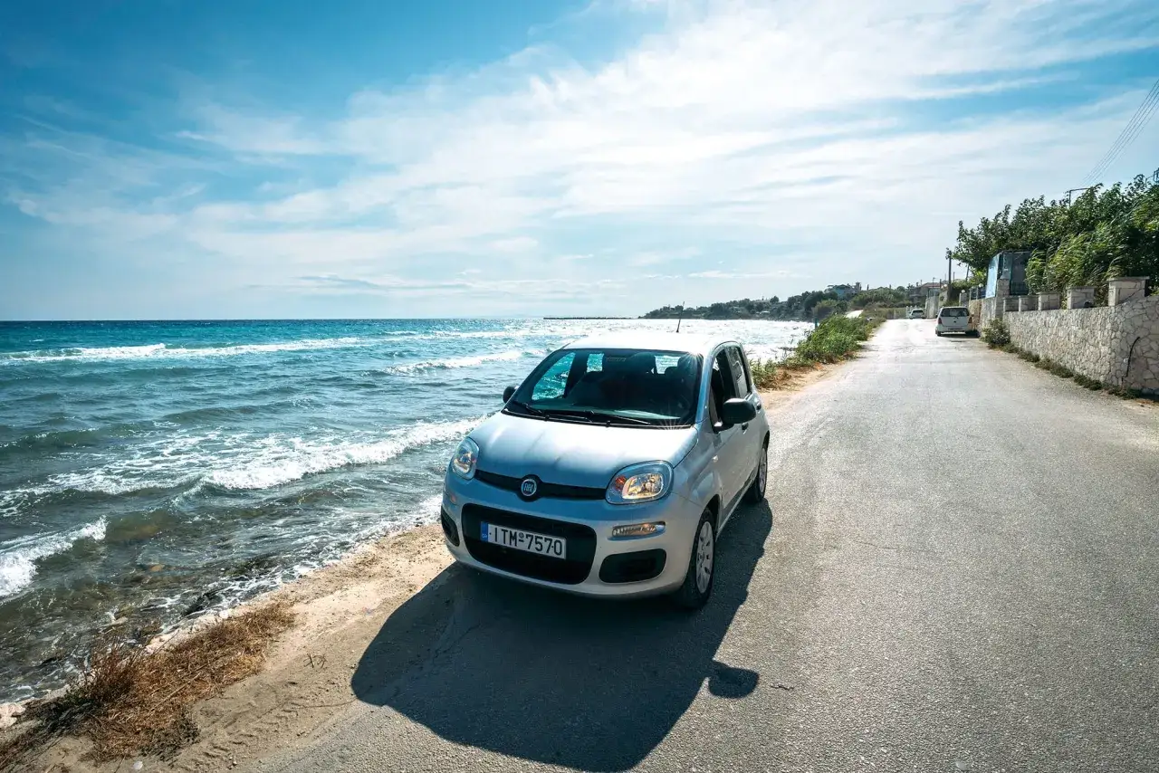 Silver Fiat Panda parked by the sea in Greece. Learn about renting a car in Greece requirements for your island adventure.