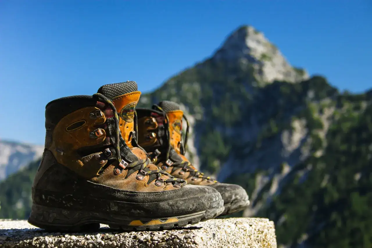 Well-worn lace hiking boots rest on a stone ledge, ready for their next mountain adventure under a clear blue sky.