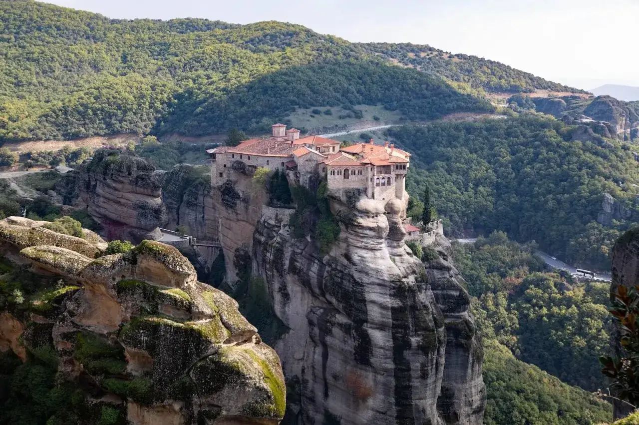 Monastery perched atop a sheer rock formation in Meteora, Greece. The ancient stone buildings with red-tiled roofs seem to defy gravity, a testament to centuries of devotion.