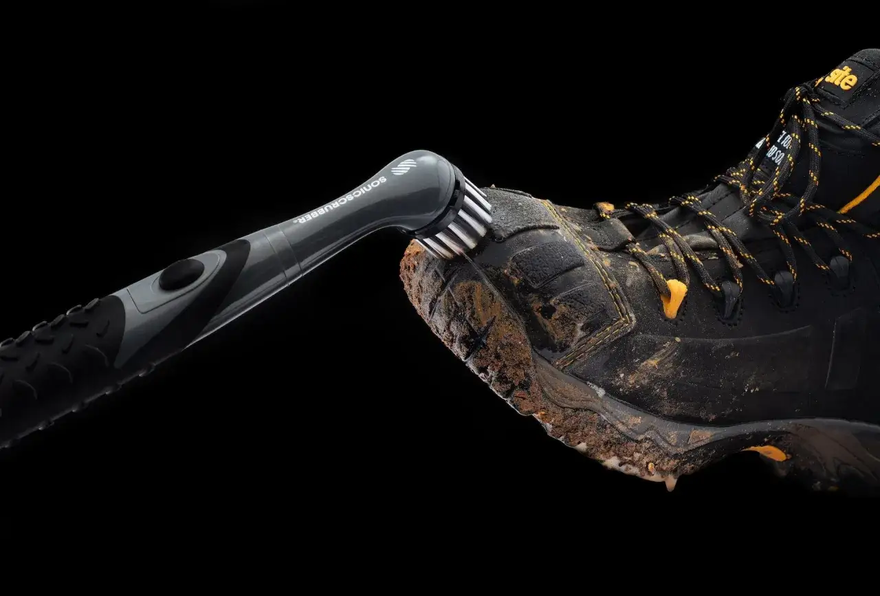 A Sonic Scrubber cleans mud off a black boot with yellow accents, showing how to clean Vibram shoes effectively.