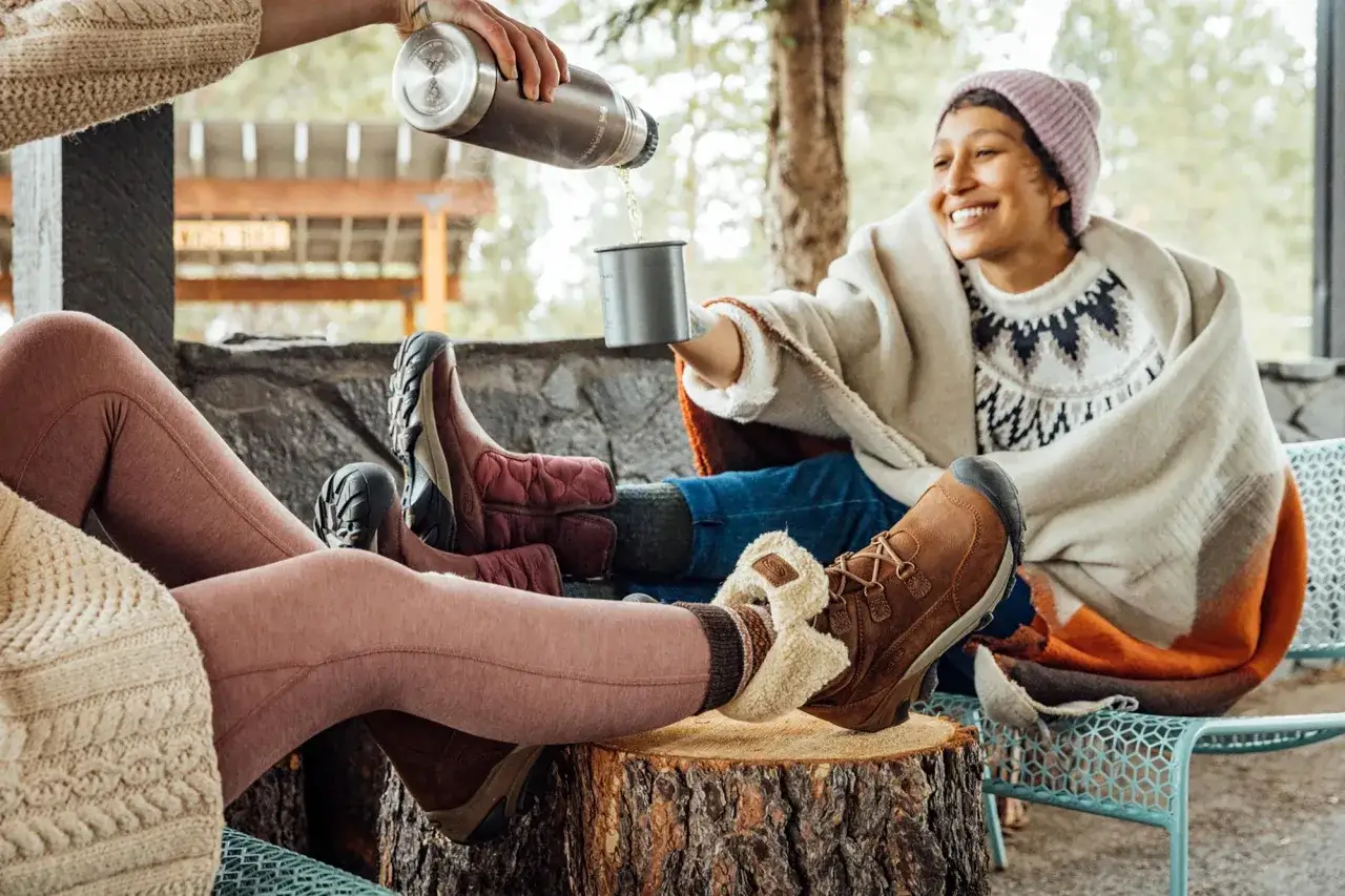 Cozy friends share warm drinks, showcasing how to keep feet warm in boots with stylish, insulated footwear perfect for chilly outdoor adventures.