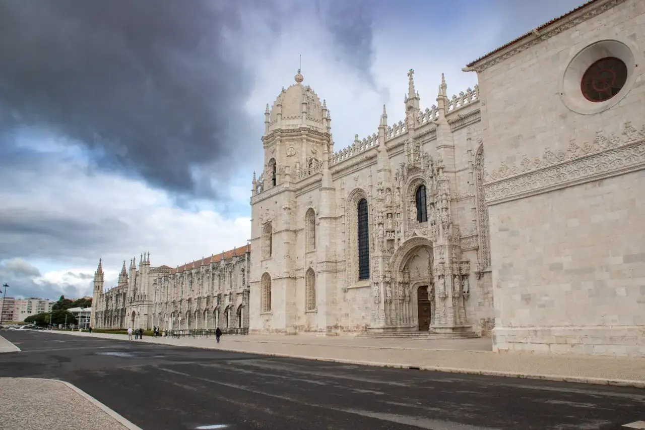 One day in Lisbon, the Jerónimos Monastery stands majestically under a dramatic sky. Its intricate stonework and grand architecture are a sight to behold.