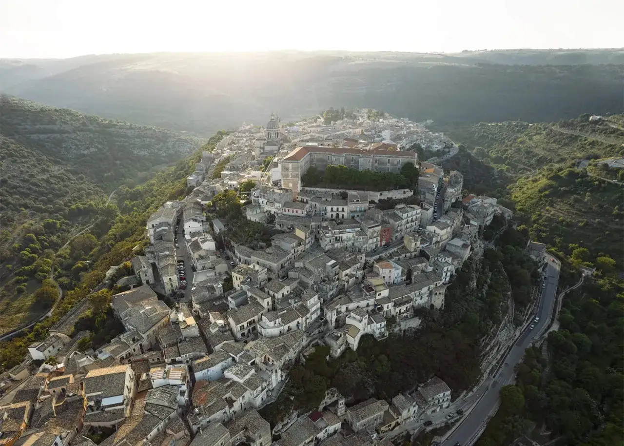 An aerial view of a hilltop town in Sicily, bathed in soft sunlight. The question 