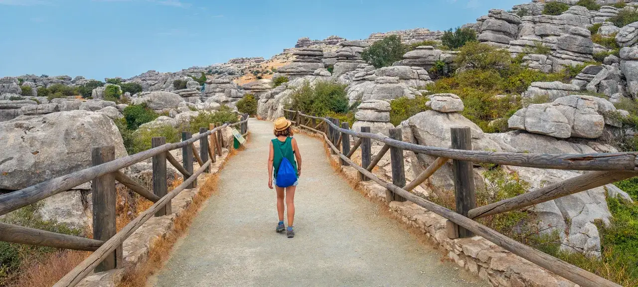 A woman enjoys walks in Spain, traversing a path through a unique rocky landscape under a clear blue sky.