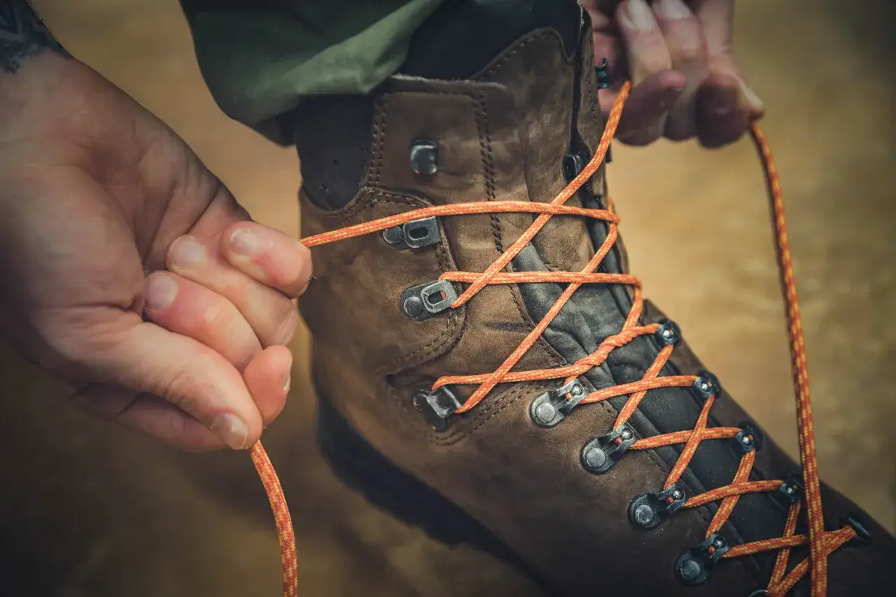 Hands lacing a brown hiking boot with orange cord. This shows how to lace hiking boots for downhill stability.