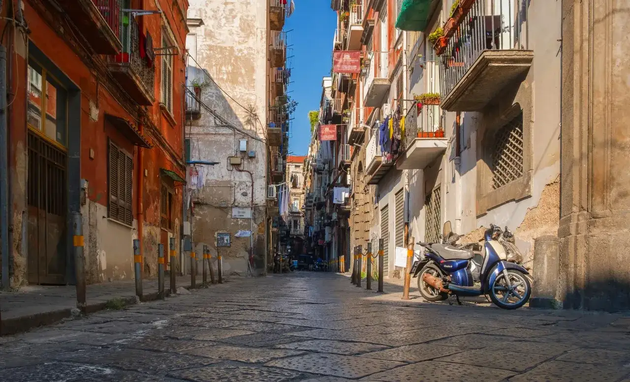 A quiet street in Naples, one day in Naples, with a blue scooter parked by a weathered building.